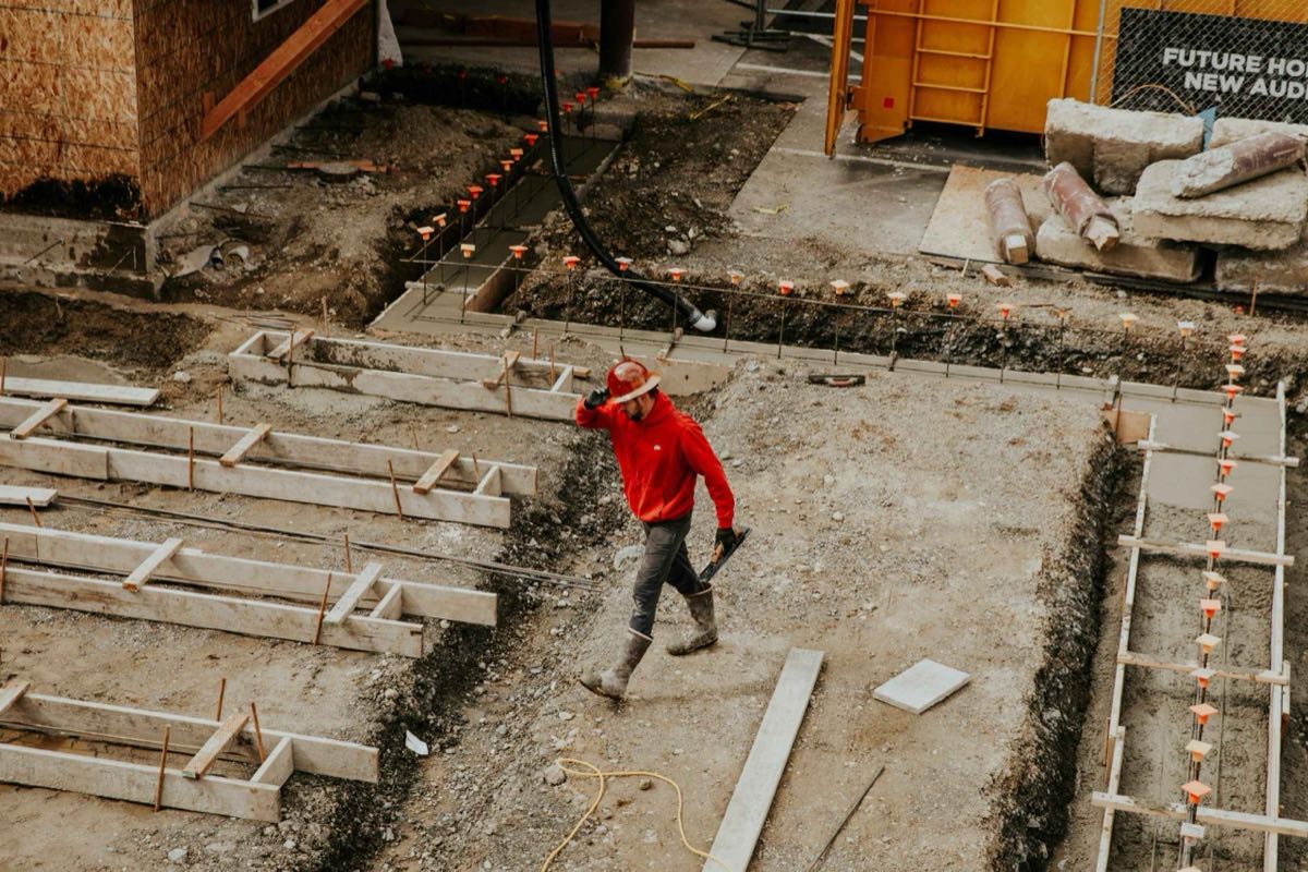 Groundworks on a construction site, with formwork laid out and a contractor in a hard hat crossing the excavation